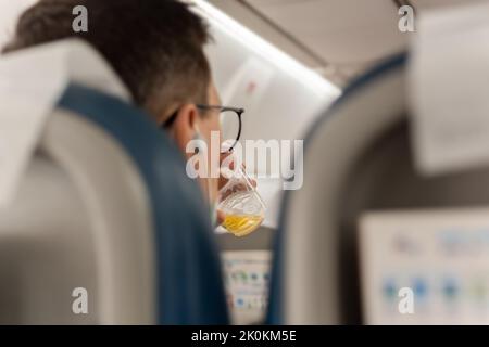 Ein männlicher Passagier entspannt sich auf einem Flug und trinkt Bier an Bord Stockfoto