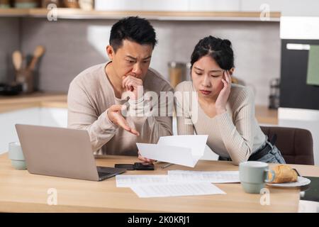 Unglücklicher asiatischer Ehemann und Ehefrau beim Lesen des Briefes, Kücheneinrichtung Stockfoto