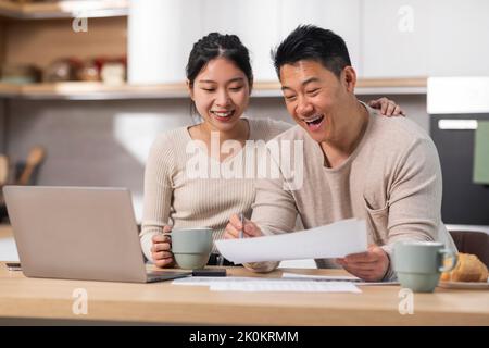 Glückliches asiatisches Paar, das mit einem Laptop im Internet Rechnungen bezahlt Stockfoto