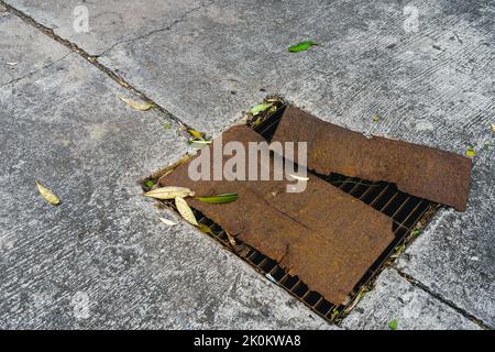 Die Ansicht der alten verrosteten Metallplatte wurde von oben verwendet, um das zerbrochene Stahlgitter der Abdeckung des Straßenabflusses zu bedecken. Verrostete Stahlblechabdeckung auf beschädigtem Ablaufgitter. Sa Stockfoto