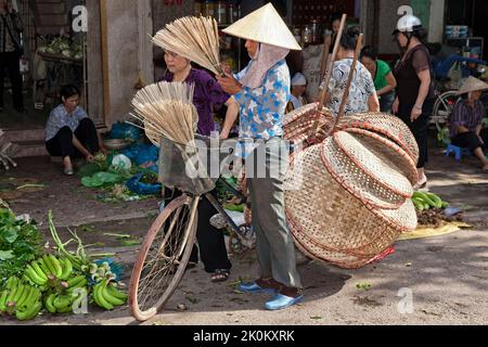 Vietnamesischer Händler mit Bambushut, der Korbartikel vom Fahrrad verkauft, arbeitet auf dem Straßenmarkt im Freien, Hai Phong, Vietnam Stockfoto