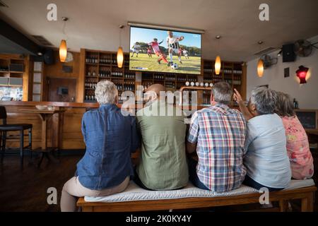 Eine Gruppe von älteren Freunden, die in der Bar sitzen und Fußballspiele anschauen Stockfoto