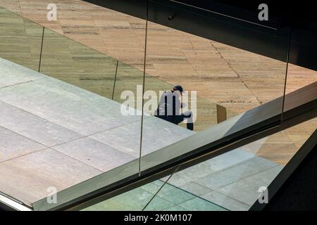 Ein Mann, der durch das Fenster eines modernen Gebäudes auf das Mobiltelefon schaute. Stockfoto