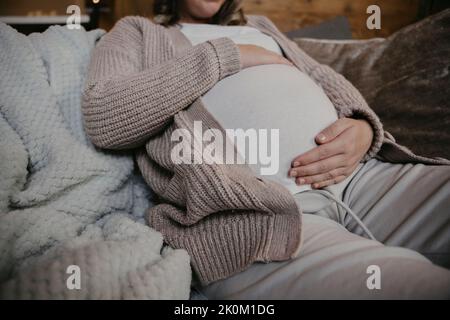 Mutter sitzt auf dem Sofa, das ihren Bauch krabelt Stockfoto