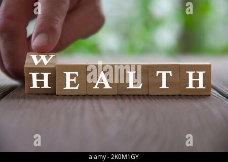 Hand Flip Holzwürfel mit Wort Reichtum zur Gesundheit mit verschwommener Natur Hintergrund. Wohlstands- und Gesundheitskonzept. Stockfoto