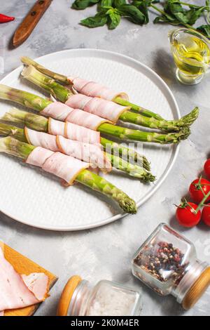 Frischer grüner Spargel, eingewickelt in Speck auf einem grauen Betontisch Stockfoto