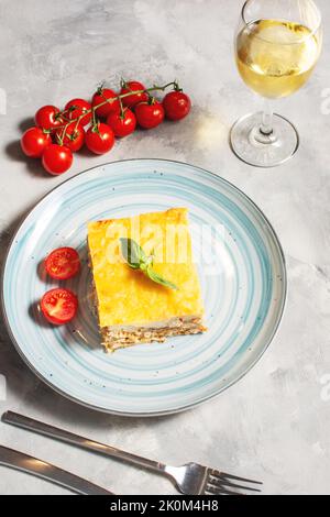 Köstliche hausgemachte italienische Lasagne mit Bachamelsauce und Gläsern Wein auf betoniertem Hintergrund Stockfoto