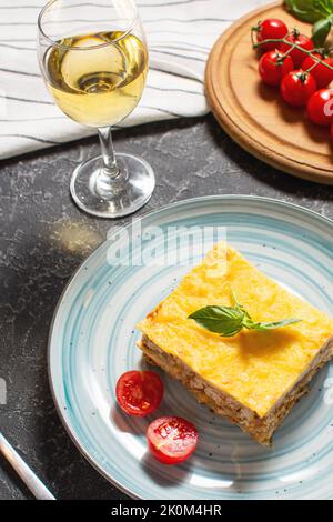 Köstliche hausgemachte italienische Lasagne mit Bachamel-Sauce und Gläsern Wein auf schwarzem Stein Hintergrund. Stockfoto