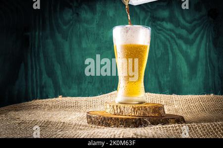 Die Bierkiste wird in einem Kristallglas auf einem blauen, strukturierten Hintergrund aus Holz serviert Stockfoto