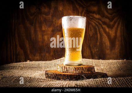 Glas mit Bier und Schaum auf dunklem Holzhintergrund Stockfoto