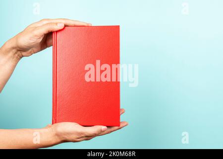 Frau Hände halten Buch mit leerem roten Deckel auf hellblauem Hintergrund. Bildung, zurück in die Schule, Selbstlernen, Buchtausch, Teilen, BookCrossing Stockfoto