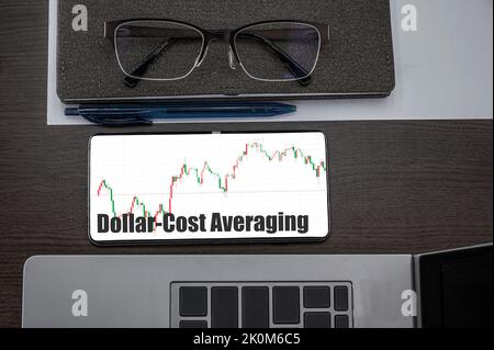 Durchschnittliche Investitionen in US-Dollar-Kosten. Draufsicht der Aktien Kurs Candlestick Chart im Telefon auf dem Tisch in der Nähe von Laptop, Notizblock und Brille. Stockfoto