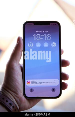 Apple iPhone 12 Pro Max in der Hand mit ios 16 und instagram-Benachrichtigung auf dem Hauptdisplay Stockfoto