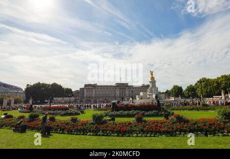 London, Großbritannien. 12. September 2022. Tausende von Menschen laufen am Buckingham Palace und dem Victoria Memorial (r) vorbei, während Gärtner die Blumenbeete pflegen. Die britische Königin Elizabeth II. Starb am 8. September 2022 im Alter von 96 Jahren. Quelle: Christian Charisius/dpa/Alamy Live News Stockfoto