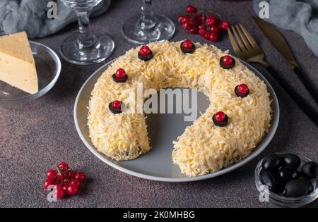 Festlicher Hufeisensalat mit Huhn, Eiern, Käse und Oliven auf braunem Tisch Stockfoto