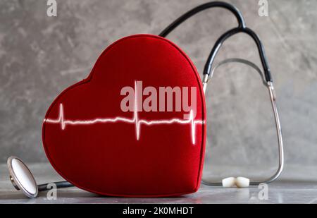 Nahaufnahme des roten Herzens, des Stethoskops und des Herzfrequenzgraphen im gleichen Bild. Konzept der kardiovaskulären Gesundheit und Krankheiten. Stockfoto