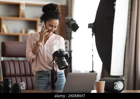 Schöne kreative Fotografin arbeitet, Telefongespräche führt, Kamera hält Stockfoto