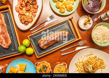 Rezepte von lateinischen Gerichten mit Käsebällchen, gegrillten Würstchen mit Zwiebeln, vom Holzkohle gegrillten Rinderstreifen und gebratener Yucca Stockfoto