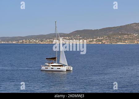 Ägina, Griechenland - Mai 2022: Modernes Katamaran-Boot, das langsam über ein ruhiges Meer vor der Küste der Insel Ägina segelt. Stockfoto