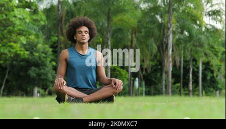 Junger afrikanischer schwarzer Mann saß auf Gras in Meditation und Kontemplation Stockfoto