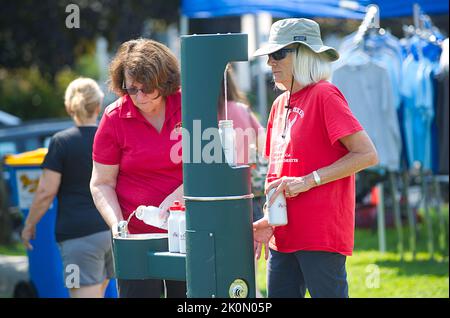 Zwei Frauen nutzen eine Tankstelle zum Nachfüllen von Wasserflaschen auf der Eastham Windmill Weekeng Messe in Cape Cod, USA Stockfoto