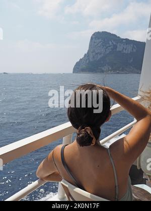Hübsche junge Frau, die ihre Augen auf der Fähre nach Capri, Kampanien, Italien vor der Sonne schützt Stockfoto