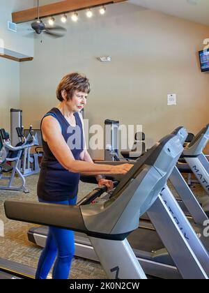 Ältere oder ältere Frau mittleren Alters, die ein Laufband in einem Fitnessstudio benutzt oder darauf läuft oder es benutzt. Stockfoto