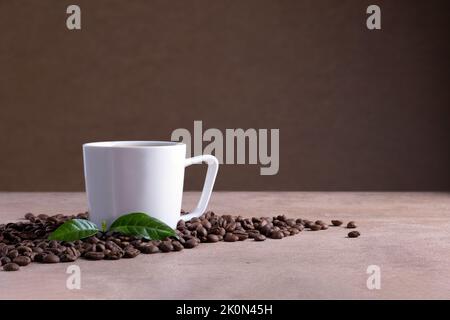 Weiße Kaffeetasse steht auf brauner Oberfläche in der Nähe von verstreuten Kaffeebohnen Stockfoto