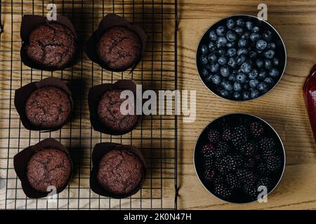 Frisch gebackene Schokoladen-Cupcakes mit Zutaten in der Nähe. Garnieren Sie mit frischen Heidelbeeren und Brombeeren Stockfoto