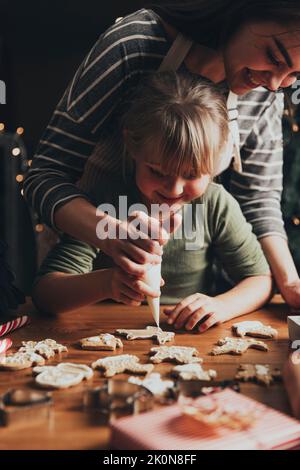 Weihnachten, Neujahr Lebkuchen Kochen, Herstellung, Dekoration frisch gebackene Cookies mit Glasur und Mastix. Mama und Kind, authentische schöne Momente. Mama hilft niedlichen kleinen Tochter zu Kekse schmücken Stockfoto