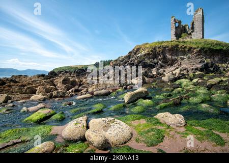 Blauer Himmel über den Ruinen von Minard Castle vom felsigen Strand von Minard Strand auf der Halbinsel Dingle aus gesehen Stockfoto