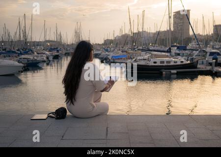 Frau auf dem Rücken, die mit Blick auf einen Hafen sitzt Stockfoto