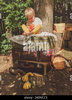 Ein kleiner Junge spielt mit einem Kürbis - sitzt auf alten Koffern Stockfoto