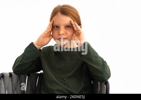 Kaukasischer hübscher Junge mit roten Haaren.modisches Bild eines Teenagers mit langen Haaren.Kind, das auf die Kamera schaut.Vorderansicht auf einem hellen Hintergrund.Studiolicht. Stockfoto