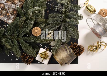 Tannenkranz und Weihnachtsdekor auf schwarz-weißem Hintergrund. Vorbereitungen für Weihnachten, Postkarte, Weihnachtskugeln, Geschenkboxen, Bänder. Flaches Lay, eleganter Stil, Urlaub. Stockfoto