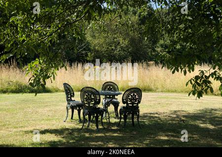 Ein Satz von grün verzierten Metalltischen und Stühlen auf einem Rasen unter dem Schatten eines Baumes in einem ländlichen Garten im Sommer. England, Großbritannien Stockfoto