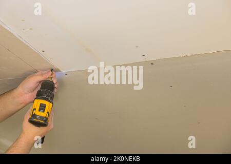 Mit einem Schraubendreher befestigt der Arbeiter die Trockenwand mit Hilfe eines Arbeiters an der Decke Stockfoto