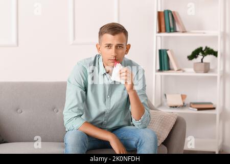 Junger Mann mit Nasenbluten und Gewebe zu Hause Stockfoto