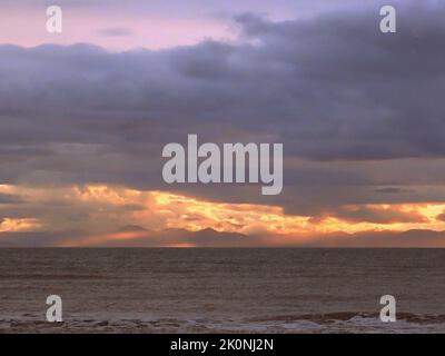 Die Sonnenuntergangsstrahlen schießen durch niedrige Wolken über dem Gipfel der Südinsel, Neuseeland, aus der Sicht des Raumati-Strandes auf der unteren Nordinsel Stockfoto