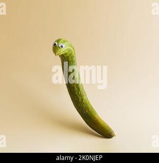 Lustige Gurke mit Augen auf beigem Hintergrund. Halloween Feiertagsidee. Kreatives Stillleben, Platz zum Kopieren. Stockfoto