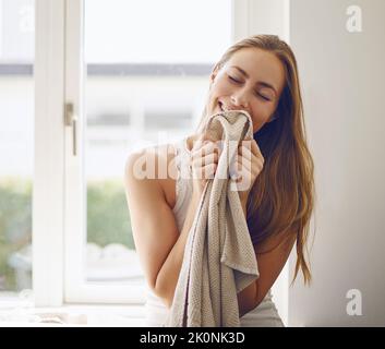 Sie riechen absolut sauber und frisch. Eine junge Frau riecht zu Hause frische Wäsche. Stockfoto