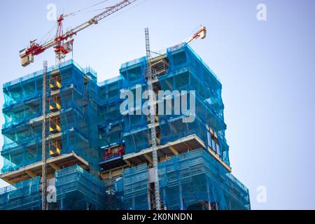 Die Fassade des zweistöckigen Gebäudes ist mit einem schützenden Konstruktionsgewebe auf blauem Himmel bedeckt. Bau von Wohngebäuden, Hausrenovierung Stockfoto