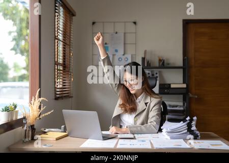 Erfolgreiche junge asiatische Geschäftsfrau Ziele erreichen aufgeregt erhobenen Hände jubeln mit Laptop auf Wokrplace im Büro. Stockfoto