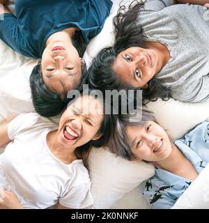 Glückliche, multiethnische junge Frauen liegen im Bett, lächeln und lachen. Draufsicht. Stockfoto