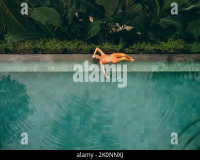 Blick von oben auf die wunderschöne Frau, die am Pool liegt. Frau im Bikini, die sich am Rande des Swimmingpools des Ferienortes entspannt. Stockfoto