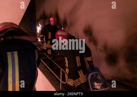 Der tapfere Feuerwehrmann steigt die Treppe eines brennenden Gebäudes hinab und hält das gerettete Mädchen in seinen Armen. Offenes Feuer und ein Feuerwehrmann im Hintergrund. Stockfoto