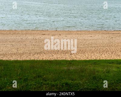 Wasser-, Sand- und Grasstreifen am Strand. Abstrakte Naturfarben an einer Uferlinie. Blaue, gelbe und grüne Töne der verschiedenen Bodenmaterialien. Stockfoto