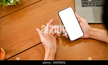 Oben ein Mann, der ein Smartphone an seinem Schreibtisch benutzt. Handy-Modell mit weißem Bildschirm in der Hand eines Mannes. Stockfoto