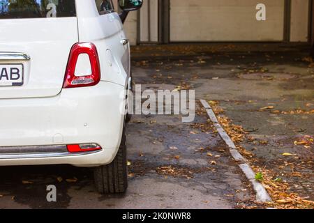 Fragment eines kompakten weißen kleinen Pkw auf einem Bürgersteig geparkt. Subkompaktes Fahrzeug für komfortable tägliche Fahrten in der Stadt. Roter Kopf hinten rechts Stockfoto