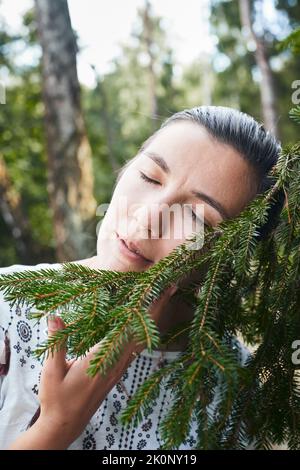 Eine Frau umarmt einen Nadelbaum im Wald. Das Konzept des Lebens in der Nähe von Natur und Wald. Vertikales Foto. Stockfoto